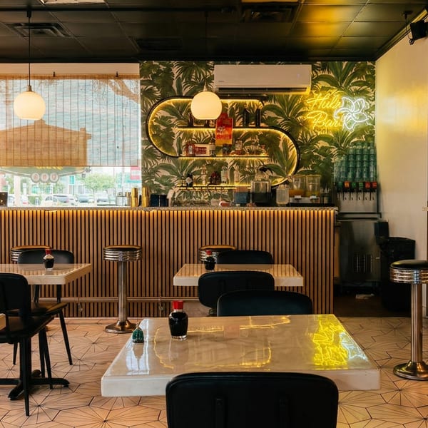 A vibrant restaurant interior with tropical wallpaper, a neon sign, and modern seating.