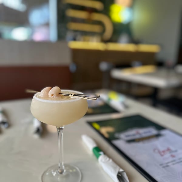 A lychee martini with two lychees on a skewer, next to a menu on a white table.