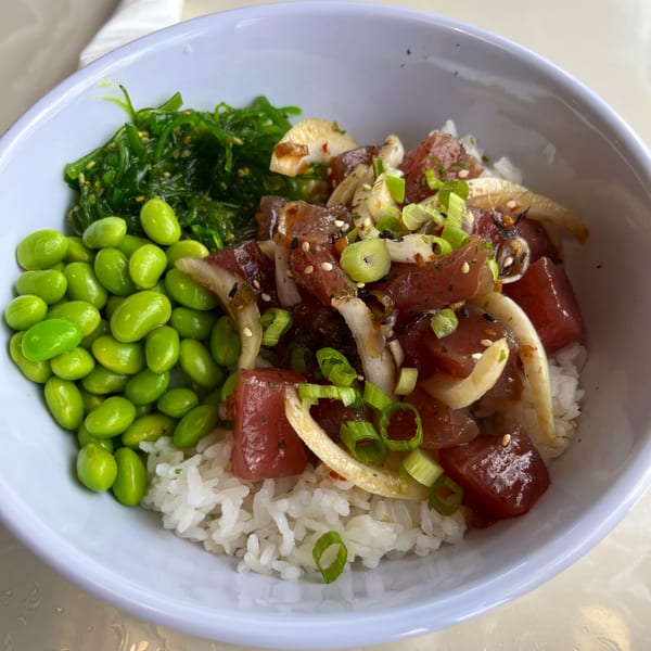 A vibrant poke bowl with tuna, edamame, seaweed salad, and rice in a white bowl.