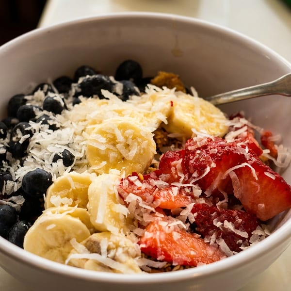 A white bowl filled with blueberries, sliced bananas, strawberries, and shredded coconut, with a spoon.